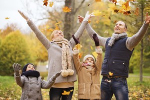 family, childhood, season and people concept - happy family playing with autumn leaves in park